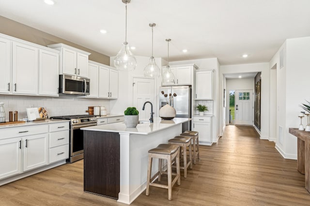 kitchen featuring a center island with sink, stainless steel appliances, hanging light fixtures, and white cabinets