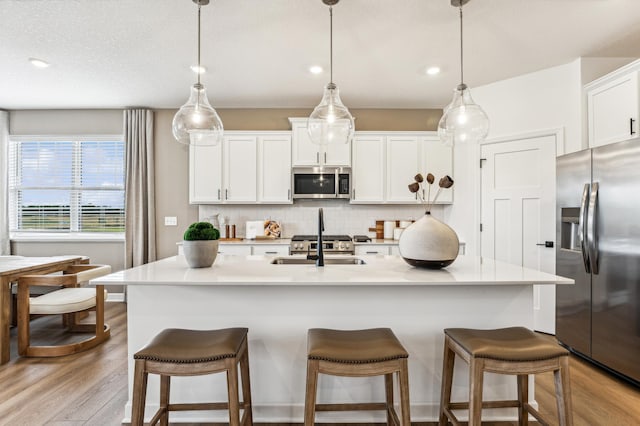 kitchen featuring appliances with stainless steel finishes, a center island with sink, tasteful backsplash, white cabinets, and pendant lighting