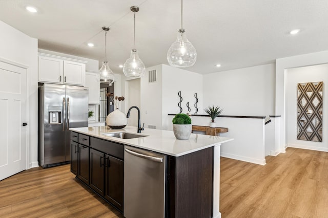 kitchen with stainless steel appliances, an island with sink, white cabinets, decorative light fixtures, and sink