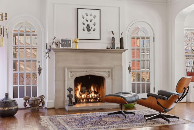 sitting room with a warm lit fireplace, arched walkways, and wood finished floors