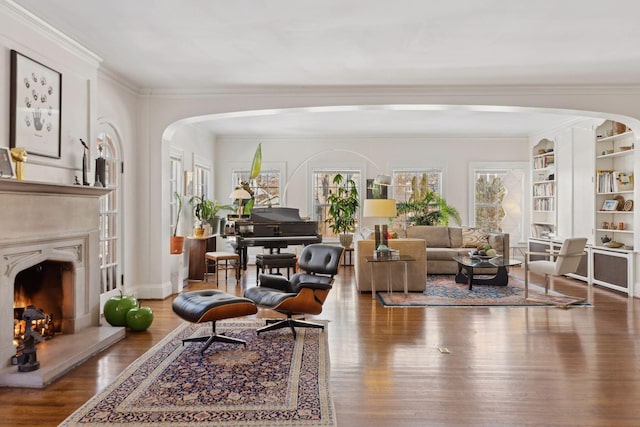 living area with arched walkways, wood finished floors, a high end fireplace, built in features, and crown molding