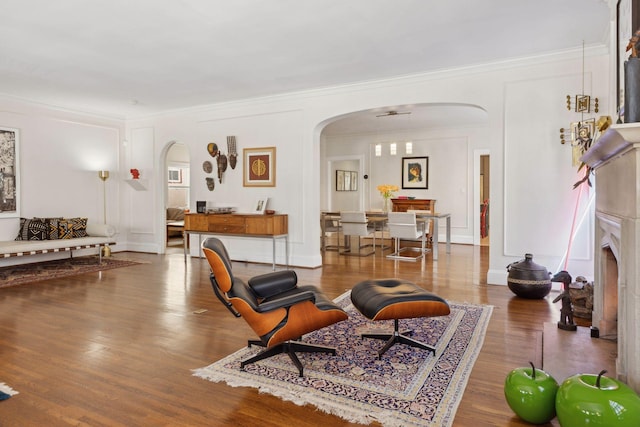 living area featuring arched walkways, crown molding, baseboards, and wood finished floors