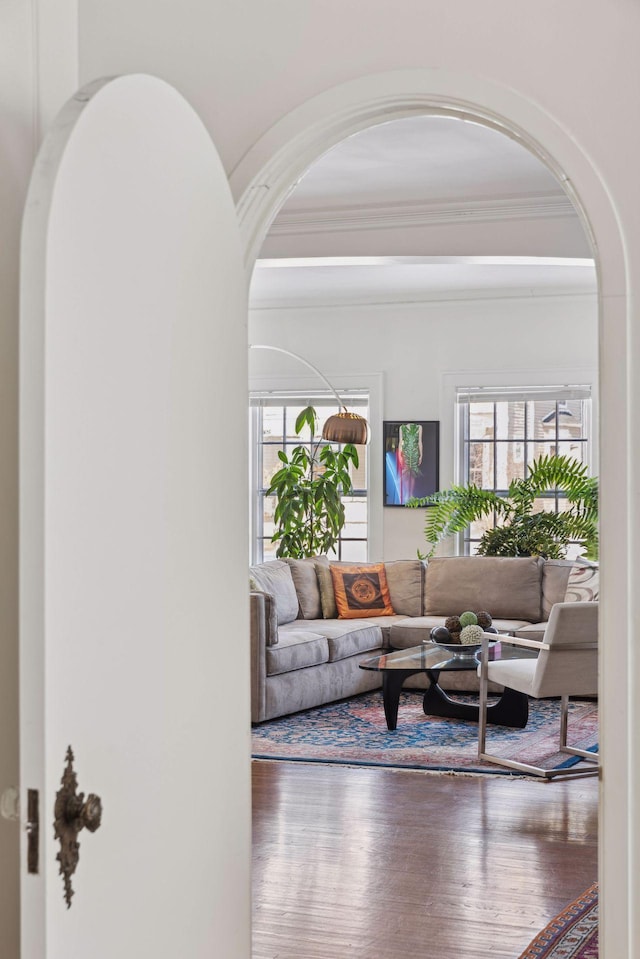 living area with ornamental molding, arched walkways, and wood finished floors