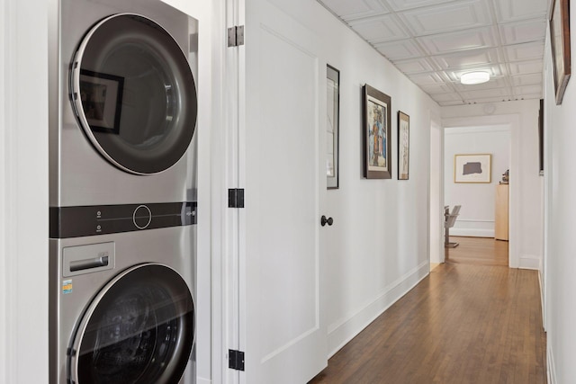 washroom featuring an ornate ceiling, stacked washer and clothes dryer, dark wood-style flooring, laundry area, and baseboards