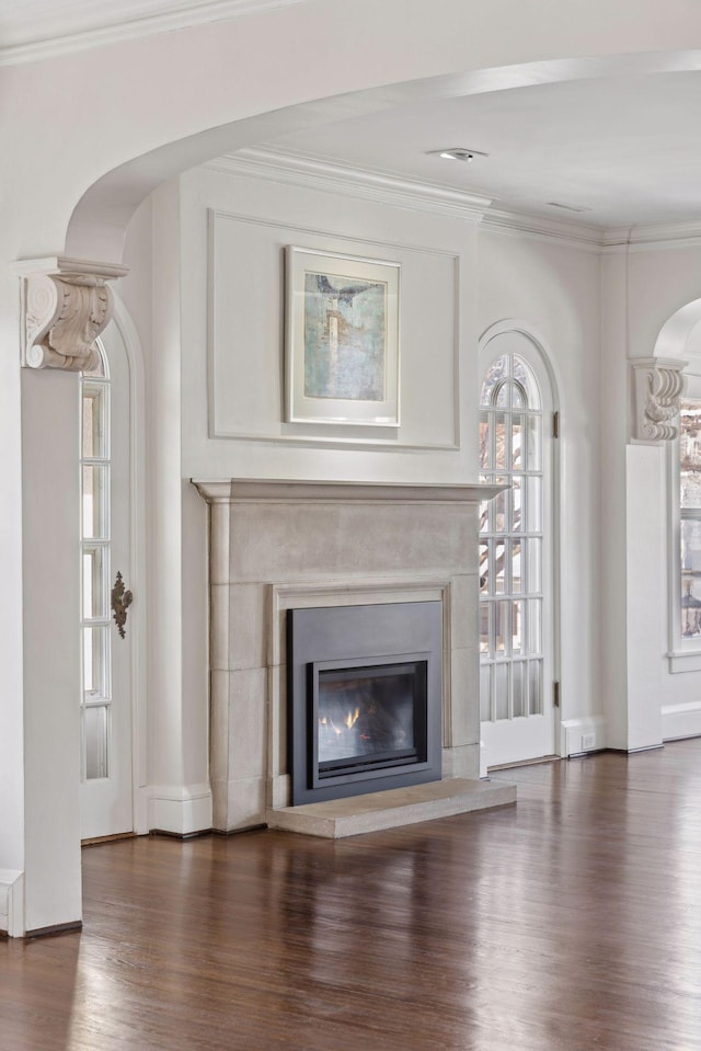 unfurnished living room featuring dark wood-style floors, a glass covered fireplace, crown molding, and arched walkways