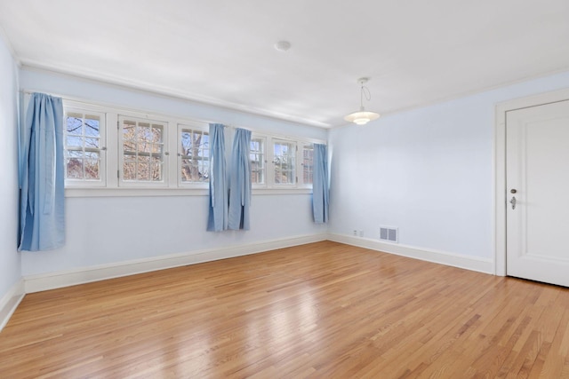 empty room with baseboards, visible vents, and light wood finished floors