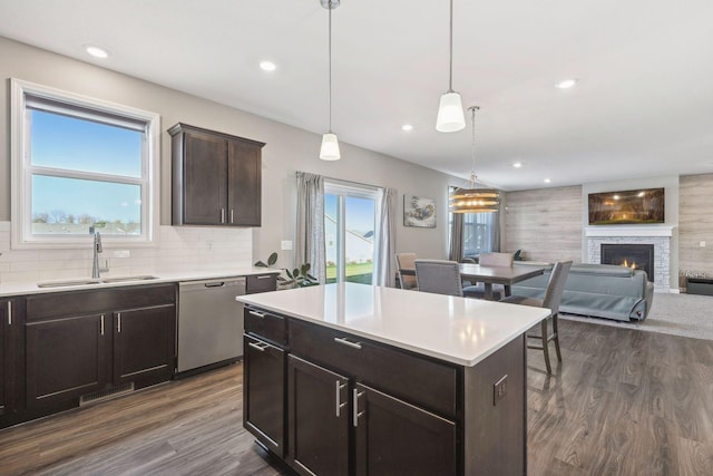 kitchen featuring hanging light fixtures, dark brown cabinets, stainless steel dishwasher, a center island, and sink