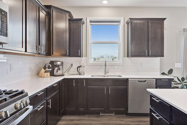 kitchen featuring stainless steel appliances, dark brown cabinetry, decorative backsplash, sink, and dark hardwood / wood-style floors