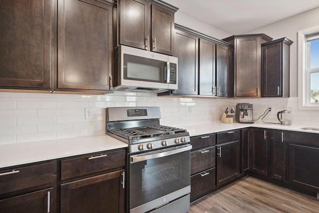 kitchen featuring dark brown cabinetry, light wood-type flooring, stainless steel appliances, and tasteful backsplash