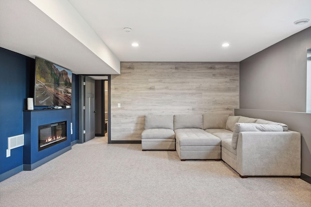 carpeted living room featuring a large fireplace and wooden walls