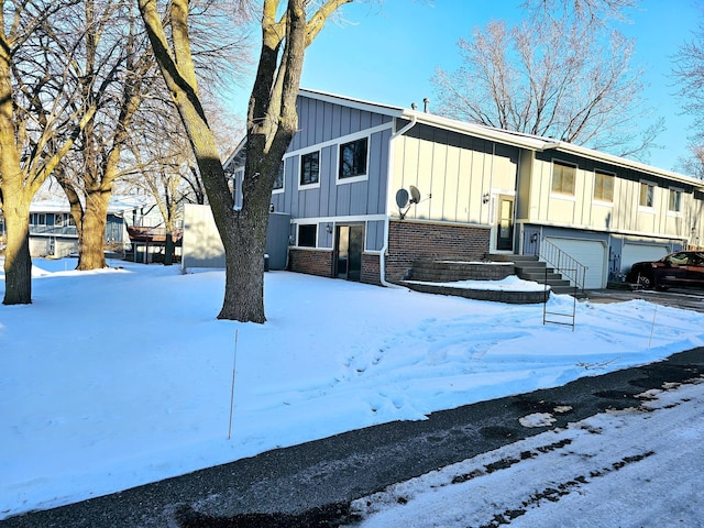 view of snow covered exterior with board and batten siding, brick siding, and a garage