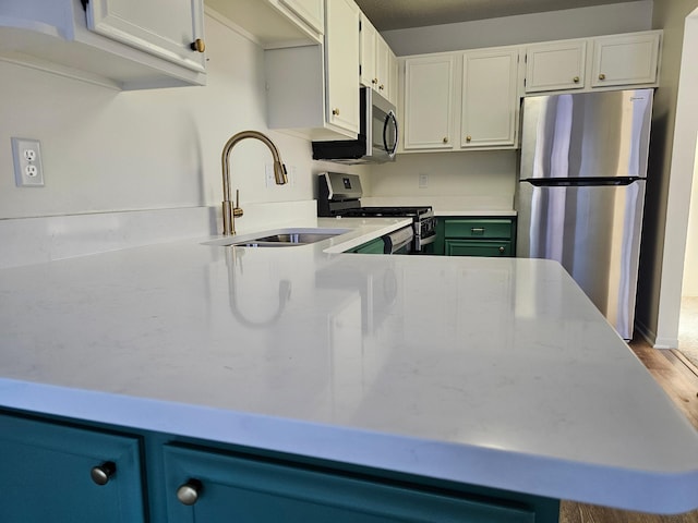 kitchen featuring stainless steel appliances, wood finished floors, a sink, white cabinetry, and light countertops