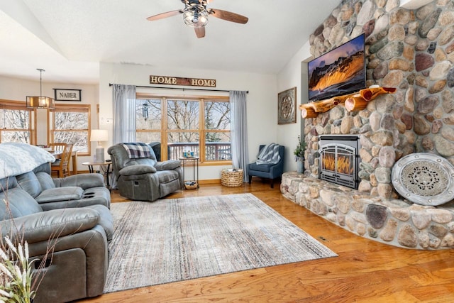 living room with lofted ceiling, ceiling fan, a stone fireplace, and wood finished floors