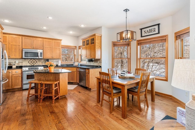 kitchen with stainless steel appliances, a center island, dark countertops, glass insert cabinets, and pendant lighting