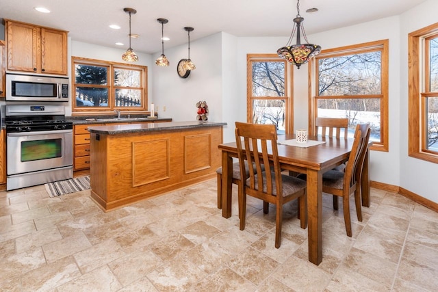 kitchen featuring stainless steel appliances, brown cabinetry, decorative light fixtures, and baseboards