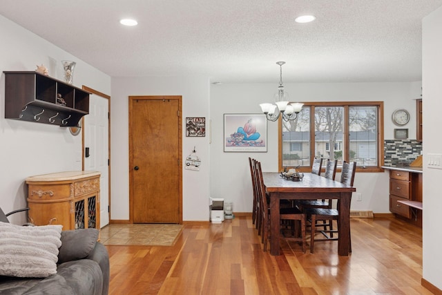 dining room featuring light wood-style floors, a textured ceiling, baseboards, and a notable chandelier