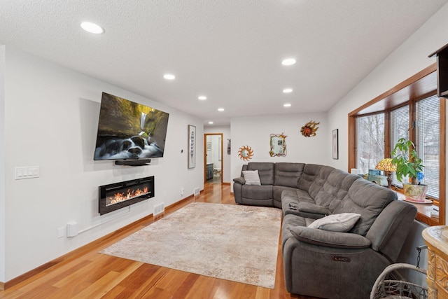 living area featuring a textured ceiling, recessed lighting, visible vents, light wood-style floors, and a glass covered fireplace