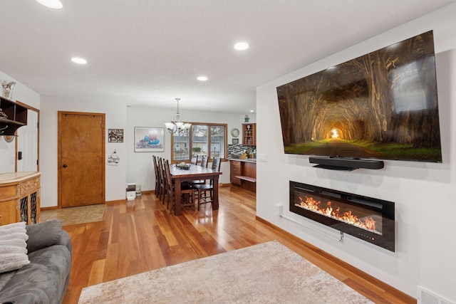 dining room featuring baseboards, visible vents, a glass covered fireplace, wood finished floors, and a notable chandelier