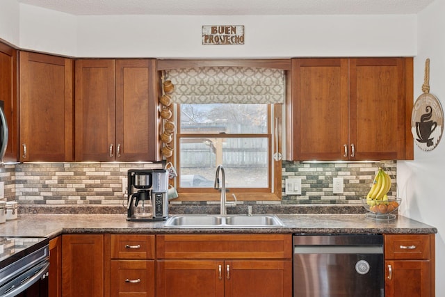 kitchen featuring brown cabinets, stainless steel appliances, dark countertops, a sink, and a textured ceiling