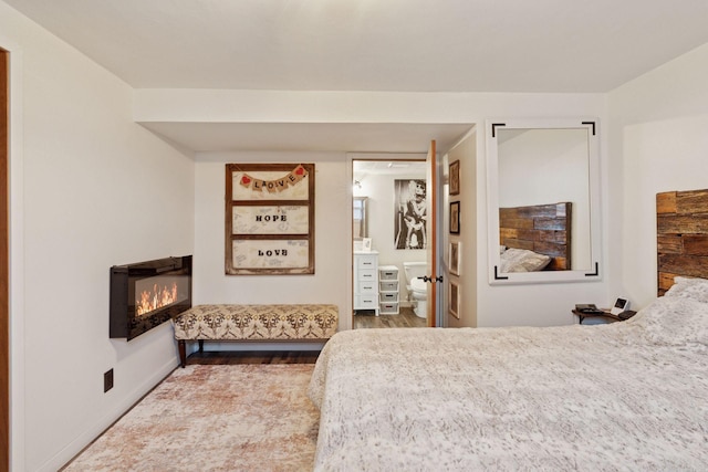 bedroom featuring wood finished floors and a glass covered fireplace