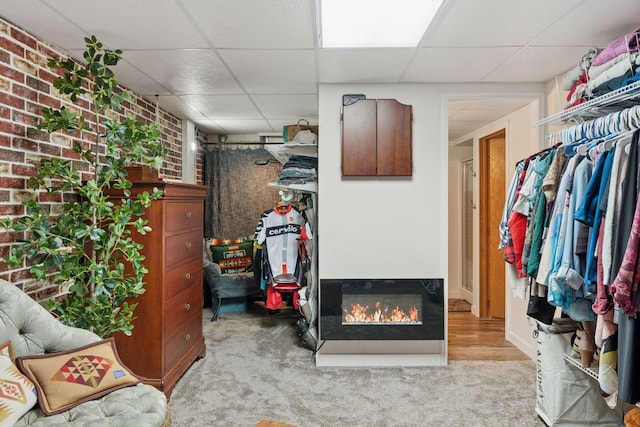 interior space featuring brick wall, carpet, a glass covered fireplace, and a paneled ceiling