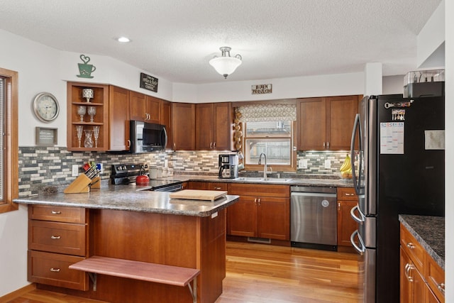 kitchen featuring light wood finished floors, open shelves, appliances with stainless steel finishes, a sink, and a peninsula