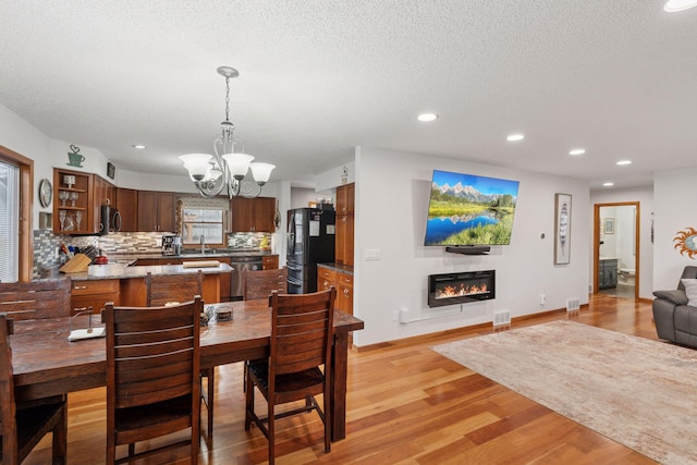 dining space with a chandelier, light wood-type flooring, a glass covered fireplace, and recessed lighting