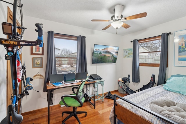 bedroom with a ceiling fan, a textured ceiling, baseboards, and wood finished floors