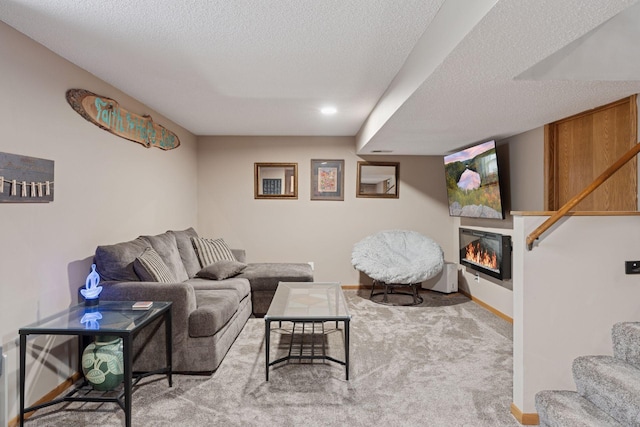 carpeted living room with a textured ceiling, stairway, a glass covered fireplace, and baseboards