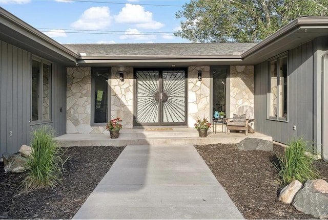 entrance to property with stone siding, roof with shingles, and covered porch