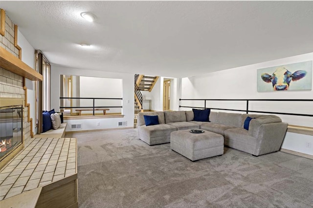 carpeted living room featuring visible vents, a textured ceiling, a brick fireplace, and stairway