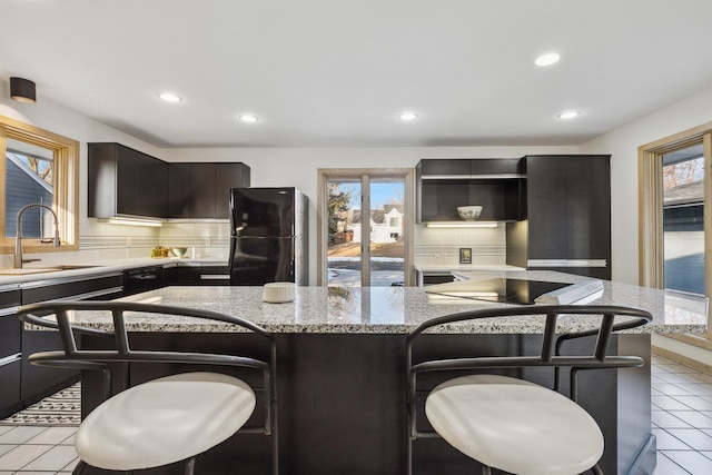 kitchen with a sink, decorative backsplash, black appliances, and a breakfast bar area