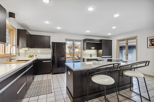 kitchen featuring a breakfast bar, a sink, a center island, freestanding refrigerator, and decorative backsplash