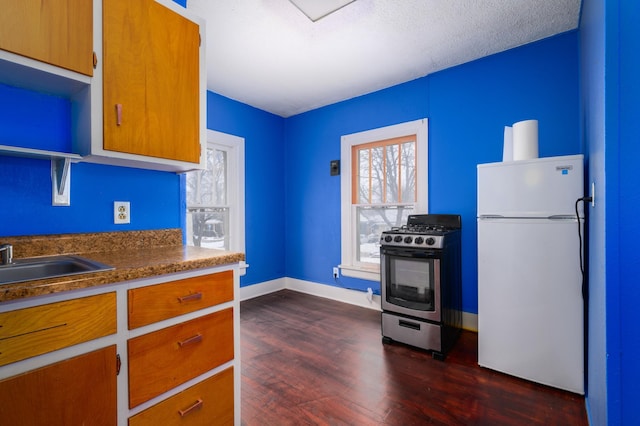 kitchen featuring white fridge, dark wood-type flooring, stainless steel gas stove, and sink