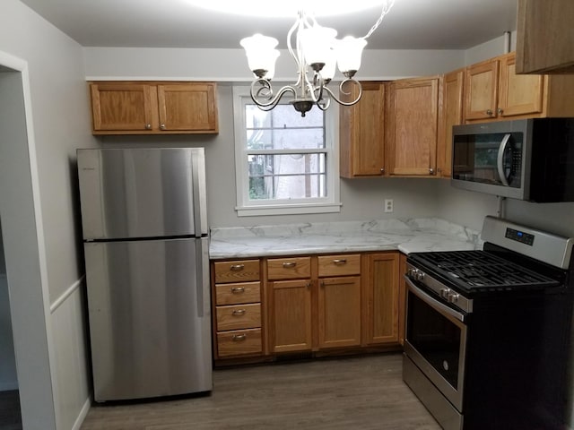 kitchen featuring dark wood-type flooring, light stone counters, stainless steel appliances, and a notable chandelier