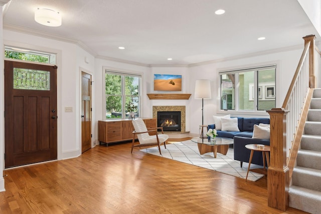 foyer with light wood finished floors, a glass covered fireplace, ornamental molding, stairs, and recessed lighting