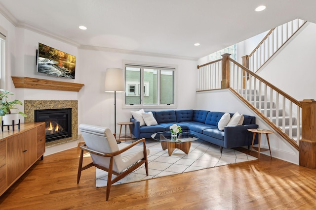 living area featuring ornamental molding, a glass covered fireplace, light wood finished floors, and stairs