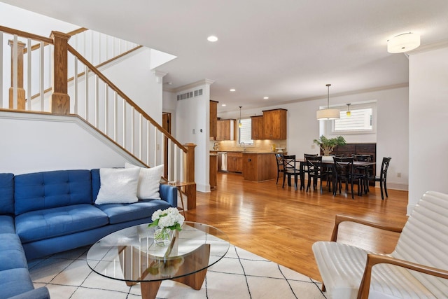 living room featuring visible vents, light wood-style flooring, stairs, crown molding, and recessed lighting