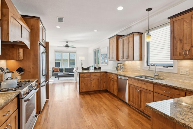 kitchen with brown cabinetry, a peninsula, hanging light fixtures, stainless steel appliances, and a sink