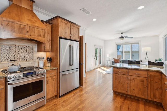 kitchen with stainless steel appliances, brown cabinetry, custom range hood, and visible vents