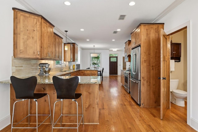 kitchen with light stone counters, appliances with stainless steel finishes, brown cabinetry, a sink, and a peninsula