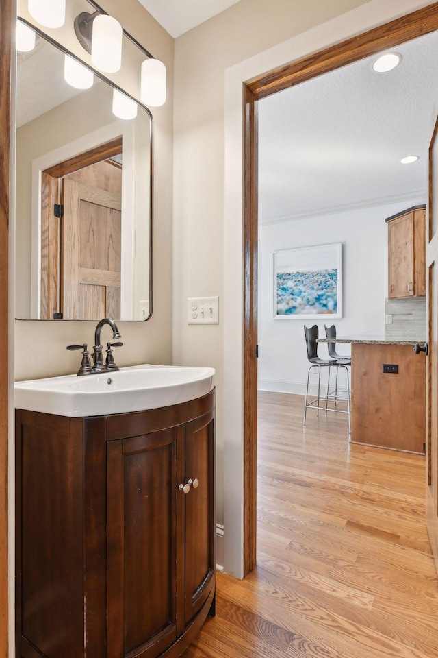 bathroom with baseboards, wood finished floors, vanity, and decorative backsplash