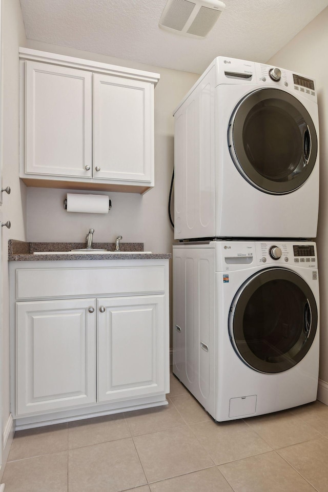 washroom featuring stacked washer and dryer, cabinet space, visible vents, a sink, and light tile patterned flooring