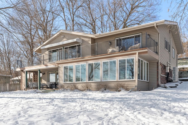 snow covered back of property with a balcony and fence