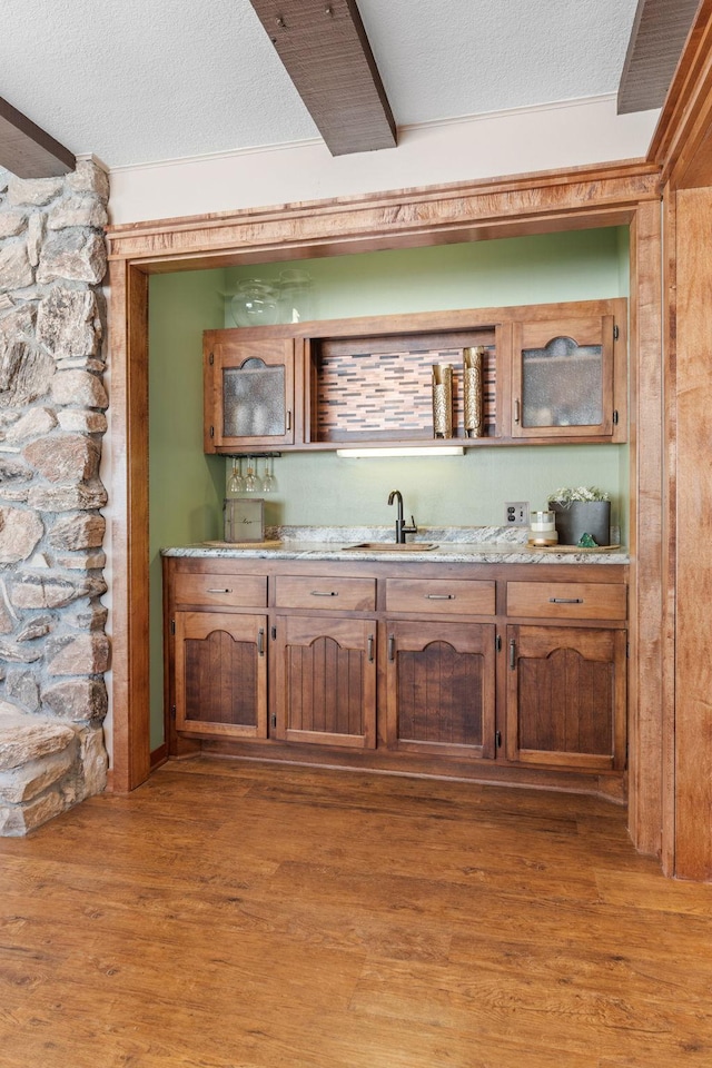 bar with a textured ceiling, light wood-style flooring, indoor wet bar, and a sink