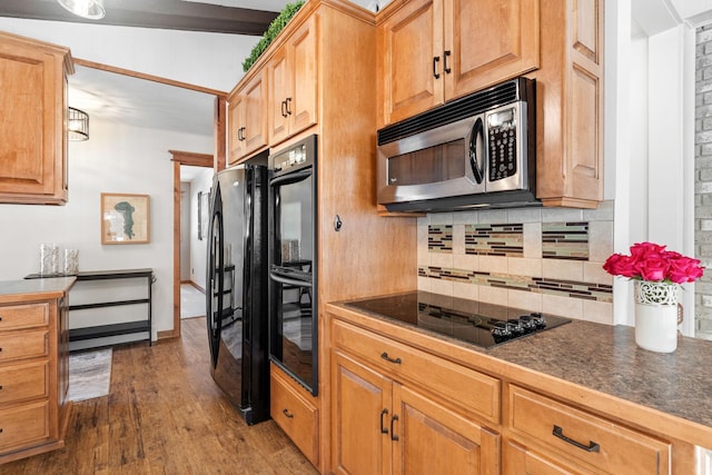 kitchen featuring dark countertops, backsplash, black appliances, and dark wood finished floors