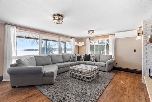 living area with a brick fireplace, a wall mounted air conditioner, a textured ceiling, and wood finished floors