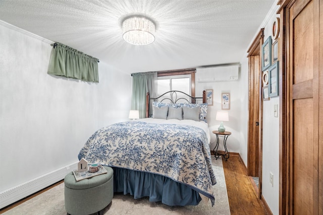 bedroom with an AC wall unit, a textured ceiling, wood finished floors, baseboards, and baseboard heating