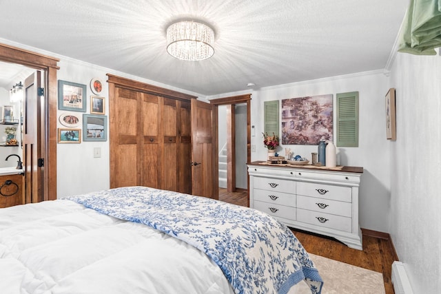 bedroom with wood finished floors, a baseboard radiator, ornamental molding, a closet, and a notable chandelier