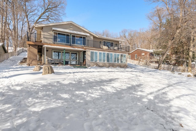 snow covered property featuring stairs, a balcony, and fence